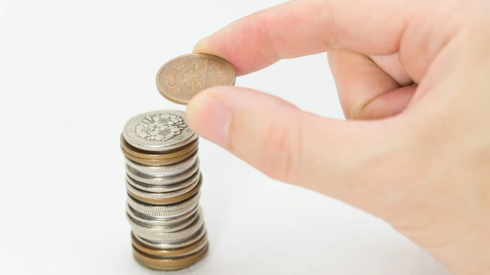 右手の親指と人差し指で100円玉の上に10円玉を乗せようとする様子