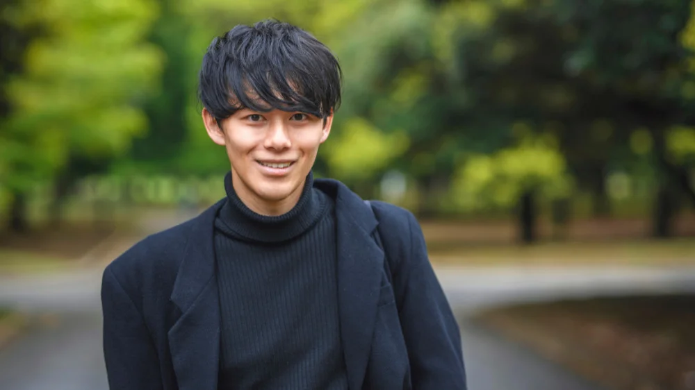 黒のハイネックの上から黒のジャケットを着ている笑顔の男性
