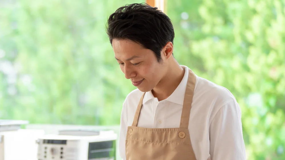 料理をしながら微笑むベージュのエプロンを着た男性