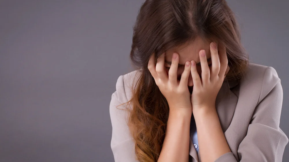 両手で顔を覆いながらうつむく女性