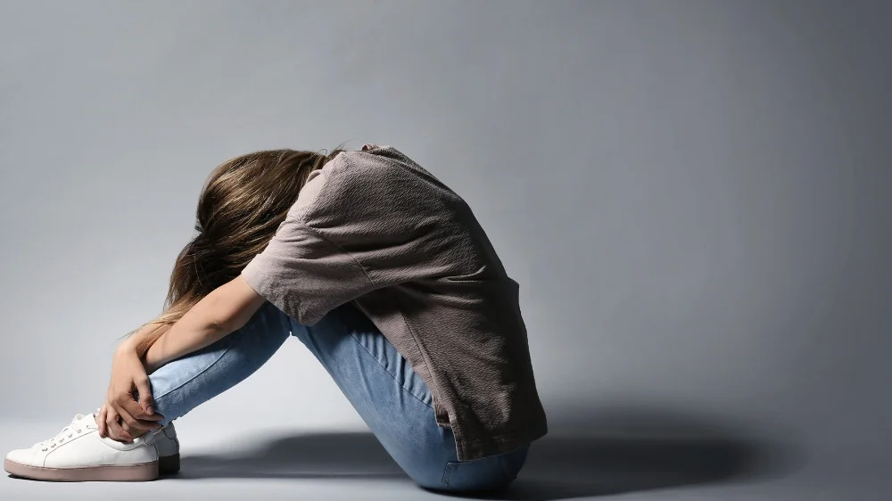 体育座りしながら下を向く白靴に青いジーンズの女性